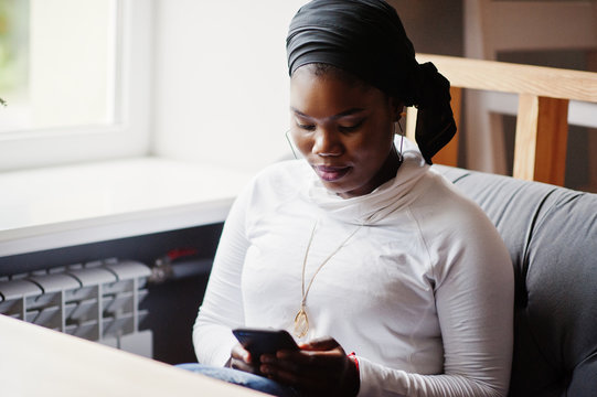 African Muslim Girl In Black Hijab Sitting At Cafe With Mobile Phone At Hand.