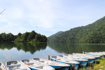 Scenery of boats lie at the bank of lake with mountain, water reflection and cloudy blue sky background.
