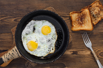 Pan of fried eggs with toasts on dark brown wooden table, top view