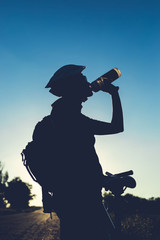 Silhouette of drinking water girl with a bicycle at sunset