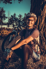 Naklejka premium Woman in helmet sitting at sunset near her bicycle