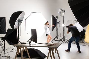 Photographer and pretty model working in modern lighting studio with many kinds of flash and...