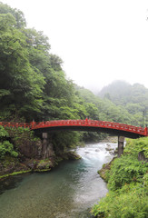 Scenery of red vintage wooden bridge over the creek with rainy sky. Vertical view.