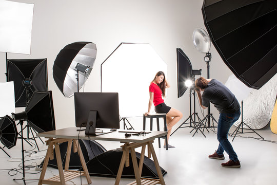 Photographer and pretty model working in modern lighting studio with many kinds of flash and accessories.