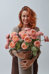 Young woman with a big vase of pink flowers around a gray background with copy space.
