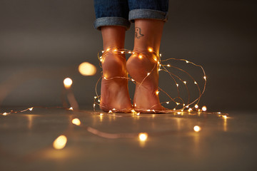 Composition of bright christmas lights decorating the feet of a young girl on a dark background