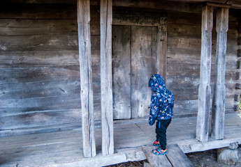 Little boy on the threshold of an old wooden house.