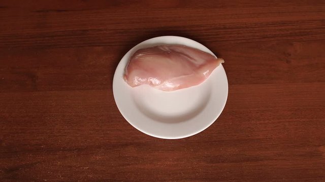 The girl puts raw chicken meat on a white plate on the table, close-up, slow motion.
