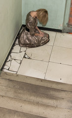 A woman in a dress sits on a concrete floor in negative feelings