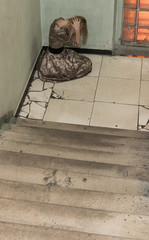 A woman sits on the concrete floor with her head in her hands, depressed