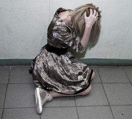 A woman sits on the concrete floor with her head in her hands, depressed