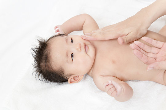 新生児の沐浴後の保湿方法を説明するマニュアル用写真。顔に保湿剤を両手の手の平でマッサージしながら塗るクローズアップ