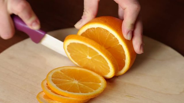 Hand slicing orange on wooden board. Woman young housewife in kitchen at home slicing fresh orange fruits on cutting board for salad or juicing. Healthy eating, cooking, dieting and people concept.