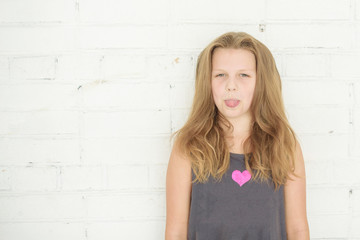 pre teen girl teen girl puts out tongue on white brick wall background