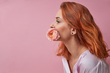 Attractive young woman holding a flower ranunculus in her mouth on a pink background