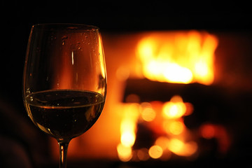 Glass with red wine on the background of fire in the fireplace, coziness and warmth at home