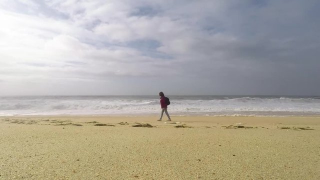 A young woman is walking on the ocean North Beach in Nazare, Portugal. Woman-traveler with a backpack.