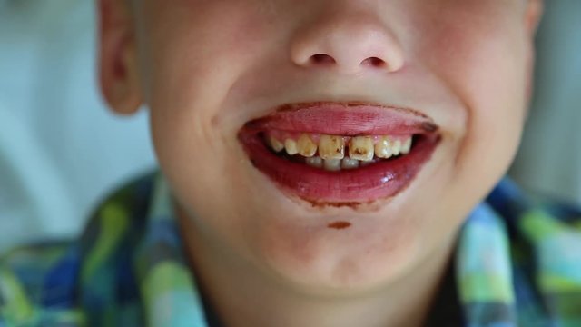 Closeup view of funny dirty mouth of kid after eating chocolate melted paste with spoon. Brown lips and teeth. Real time full hd video footage.