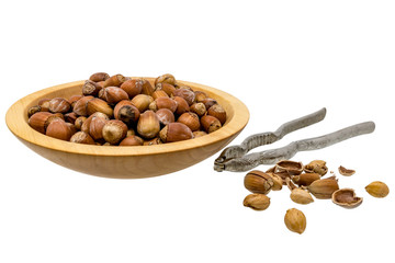 Wooden bowl with hazelnuts, nutcracker and opened nuts isolated on white