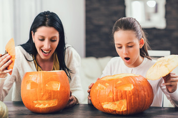 Mother with daughter creating big orange pumpkin for Halloween and having fun