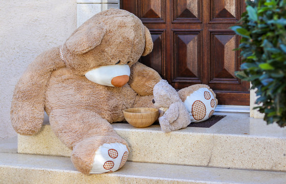Big and small Tedy Bears sitting on stairs outside of house looking into empty bowl. Friendship of opposites.