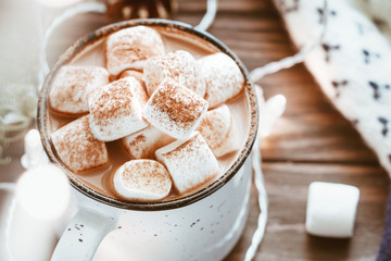 Hot cocoa with marshmallow in a white ceramic mug surrounded by winter things on a wooden table. The concept of cosy holidays and New Year.