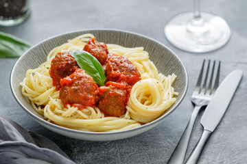 Beef meatballs in tomato sauce with Italian spaghetti and fresh basil leaf on a dinner table. Simply homemade recipe.