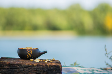 Crunchy, fried and salted peanuts, peeled. A nutritious snack in a small kerimic pot on the background of a natural brown tree with a natural pattern. Appetizing dish in the fresh air.