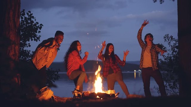 Cinemagraph loop - joyful friends multiethnic group are dancing around fire in forest during weekend trip. Young people are having fun, flame is moving.