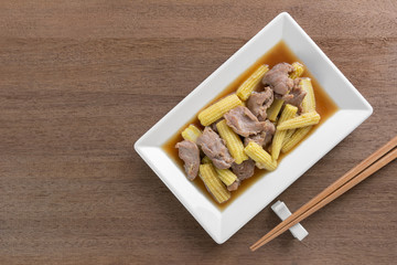 top view of stir fried baby corn and pork with oyster sauce in a plate on wooden table. asian homemade style food concept.