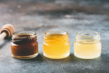 Honey in small jars and wooden honey dipper. Different types of honey. Closeup view, toned image, copy space for text