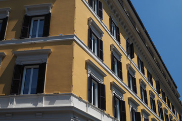 Facade of a block of flats in Rome, Italy, painted warm yellow with shuttered windows