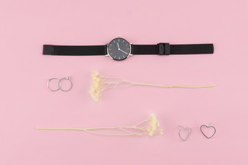 Black watch, rings and earrings decorate with white dried flowers on pastel pink background 