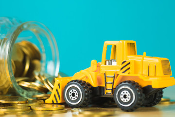 Mini bulldozer truck loading stack coin with pile of gold coin to glass jar, business finance and banking industrial concept.