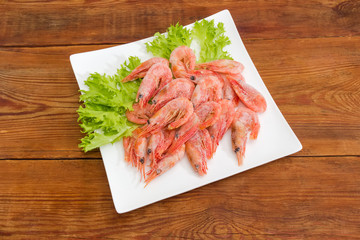 Frozen shrimps with lettuce on square dish on wooden surface
