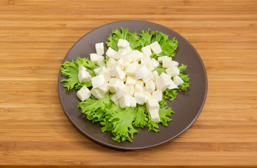 Diced mozzarella cheese on lettuce leaves on brown dish