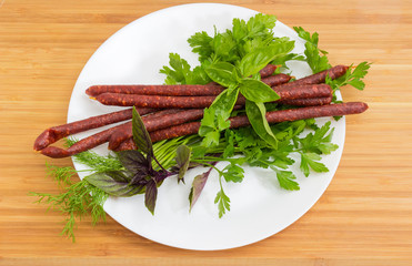 Smoked thin sausages among of greens on white dish