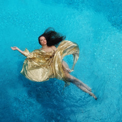 schöne junge Frau in goldenem Kleid, Abendkleid schwebt schwerelos elegant schwimmend im Wasser im...