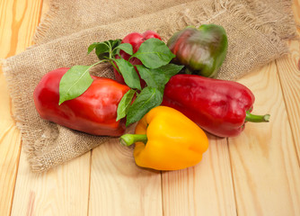 Varicolored bell peppers with twigs and leaves on wooden surface