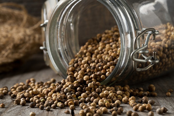 Raw, unprocessed organic coriander or cilantro seeds in glass jar on wooden table