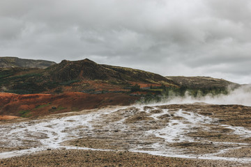 beautiful landscape with volcanic vents under cloudy sky in Haukadalur valley in Iceland