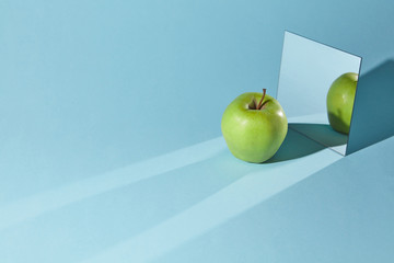 The apple is green, a square mirror on a blue background, a reflection of an apple and from shadows...