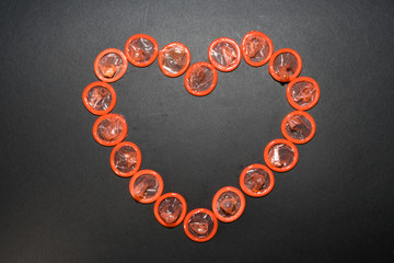 heart is laid out with orange condoms on a black background