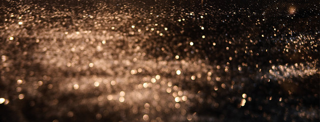 Blurred background lights. Abstract defocused gold, white, red and yellow glitters texture on black background. Shining glowing snow effects