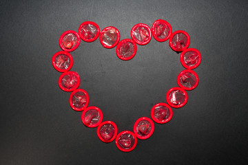 The heart is laid out with red condoms on a black background