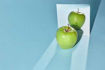 The apple is green, a square mirror on a blue background, a reflection of an apple and from shadows...