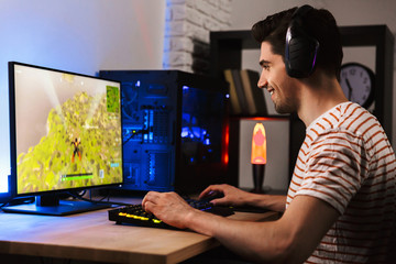 Portrait of european gamer guy playing video games on computer, wearing headphones and using...