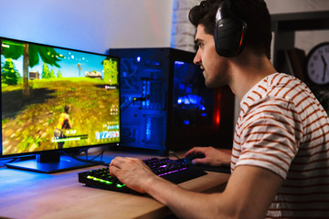 Image of young man playing video games on computer, wearing headphones and using backlit colorful keyboard © Drobot Dean