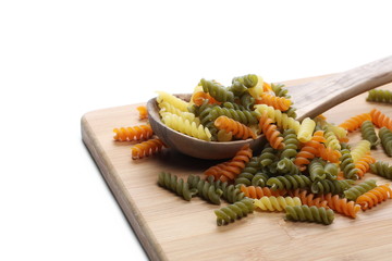 Colorful Italian spiral shaped pasta, macaroni on wooden chopping board with spoon isolated on white background