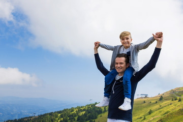 Happy father carrying son on shoulders while standing on mountain peak.
